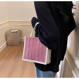 Detail of pink striped linen tote bag shown held by a model in a minimalist room
