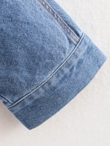 Close-up of light blue denim jacket cuff with orange contrast stitching and high density fabric
