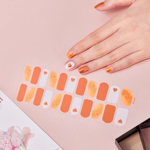 Detail of orange heart nail stickers with gold foil accents on model's fingers