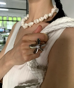 Close-up of silver flower ring with pearl and chunky white beaded necklace on a model