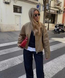 Street style detail of a khaki pilot jacket featuring silver zipper and glossy leather texture