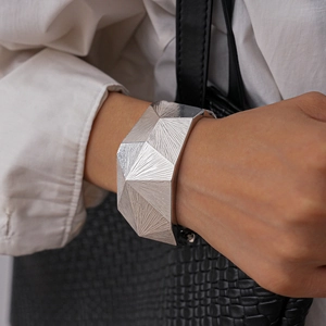 Makro-Detail des silbernen geometrischen Armreifs mit facettierten Kanten und Bürstentextur