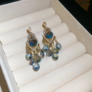 Detailed close-up of Bohemian drop earrings with blue gemstones on a beige velvet stand