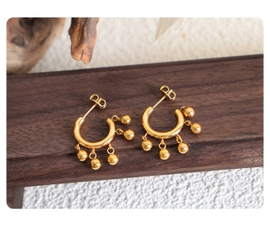 Detail of vintage C-shaped gold hoop earrings with metallic bead fringe on wood base