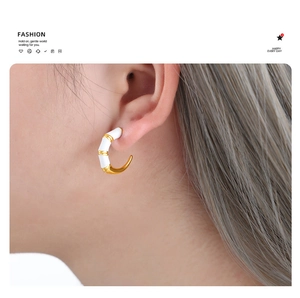 Close-up of C-shaped bamboo earrings featuring white enamel and gold textured accents