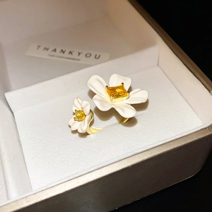 Detailed macro view of gold-plated open ring with white enamel flower and yellow zircon