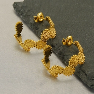 Detailed view of wave-textured C-shaped gold earrings on dark stone and grey silk
