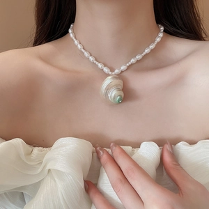 Detailed view of irregular shell conch pendant on a white pearl beaded necklace