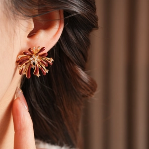 Gros plan de boucles d'oreilles feu d'artifice en émail bordeaux et zircons dorés