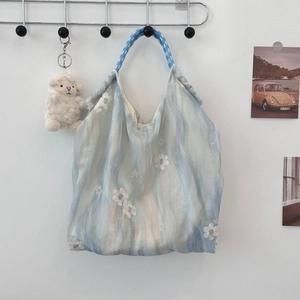 Detailed embroidery of white lace flowers on a soft blue silk tote bag with rope handle
