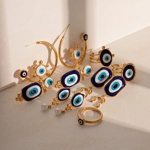 Golden Evil Eye jewelry set including earrings and rings on beige display surface