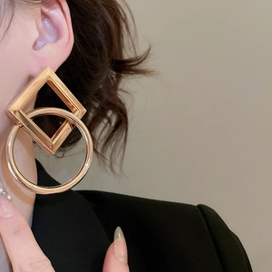 Close-up of a model wearing large gold geometric square and circle metal stud earrings