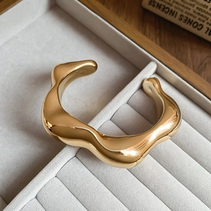 Macro detail of golden chunky wave bangle with polished mirror finish on velvet tray