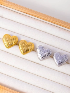 Macro shot of gold and silver heart studs with textured woven design on white velvet tray