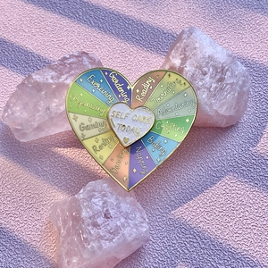 Close-up of heart enamel spinner pin with 'Self Care Today' text on pink quartz