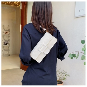 Close-up of white crocodile pattern underarm bag with decorative buckle on a model