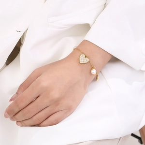 Close-up of a gold heart pendant and pearl charm bracelet worn by a model in a white blazer