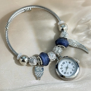 Silver beaded bracelet watch featuring owl and wing charms on a luxury champagne silk background