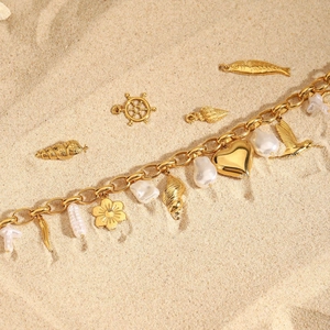 Vue détaillée du collier doré avec perle et breloques nautiques sur fond de sable