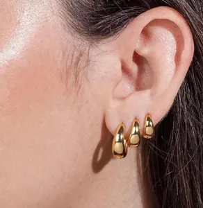Three-piece set of thick gold hoop earrings shown layered on model ear in macro detail