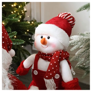 Detail of plush Christmas snowman doll with red knitted hat near festive lighted tree
