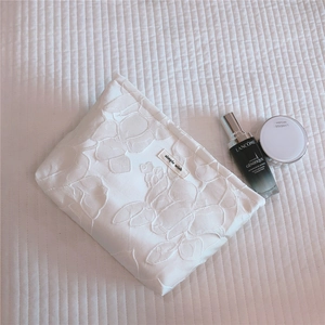 Detailed embroidery of large floral patterns on white quilted cotton cosmetic travel bag