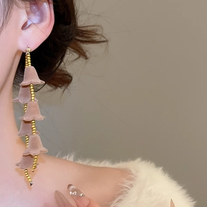 Gros plan de boucles d'oreilles fleurs floquées marron Morandi avec détails de pompons dorés
