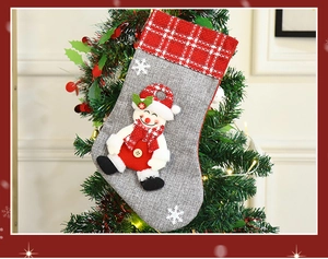 Linen snowman Christmas stocking with red plaid cuff hanging on a festive tree branch