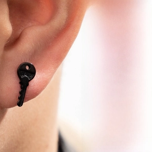 Close-up of a matte black stainless steel key shaped stud earring worn on ear