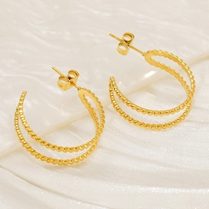 Close-up of golden double-layer hoop earrings with beaded texture on white silk background