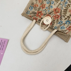 Detail of linen handbag showing floral embroidery, woven handle and wooden buckle closure