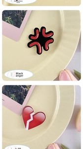 Detail view of acrylic pins featuring black angry symbol and red broken heart designs