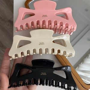 Détail de grandes pinces à cheveux en acétate rose, beige et noir avec texte doré