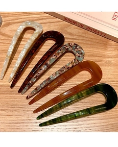 U-shaped hair pins in various colors like pearl white and tortoiseshell on a desk