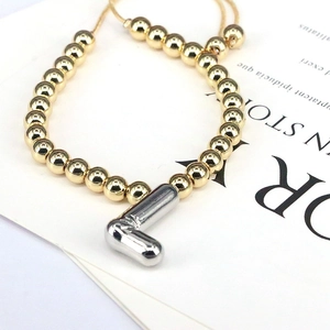 Detail of adjustable gold beaded bracelet featuring a silver balloon letter L charm