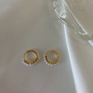 Elegant gold hoop earrings with small pearls on beige silk background, minimalist style