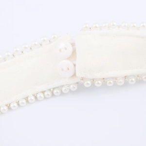 Detail showing white fabric texture with pearl trim and double button closure on dress