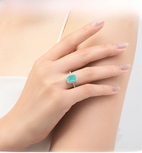 Detail of emerald-cut green gemstone ring with halo diamonds on a hand