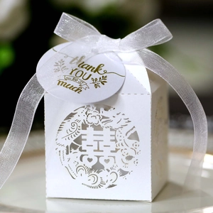 Macro shot of white laser-cut wedding favor box with gold tag and organza ribbon