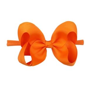 Detail of bright orange grosgrain ribbon bow on soft elastic nylon headband for babies