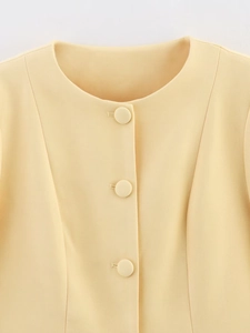 Detail von Rundhalsausschnitt und Stoffknöpfen an der hellgelben schmalen Jacke