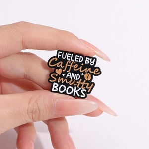 Cartoon enamel pin fueled by caffeine and books badge shown being held by fingers