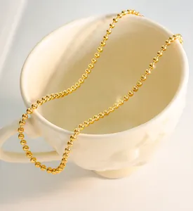 Detail einer minimalistischen goldenen Kugelkette, die an einer weißen Keramiktasse hängt