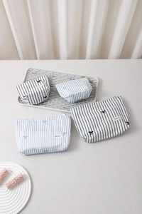 Détail de trousses à maquillage rayées avec broderie nœud et fermeture éclair en bleu
