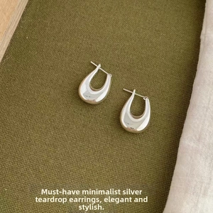 Macro shot of polished silver teardrop earrings on dark olive green textured fabric