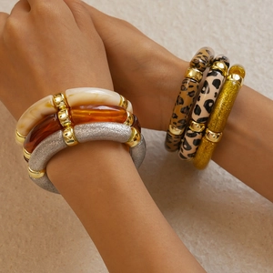 Close-up of stacked acrylic leopard print and amber resin bangles worn on a model wrist