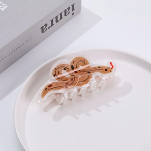 Brown snake-shaped acrylic hair claw clip with serpent pattern on a white plate