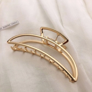 Detail of a large gold metal hair claw clip with elegant hollow lines on white fabric