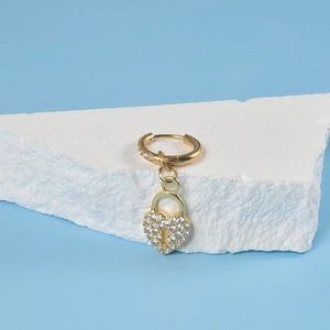Detailed close-up of gold hoop earring featuring a pavé heart lock charm on stone background