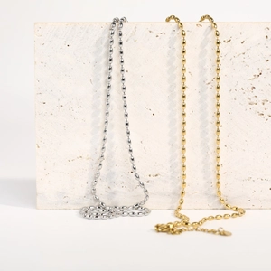 Minimalist silver and gold stainless steel bead necklaces on a textured stone base